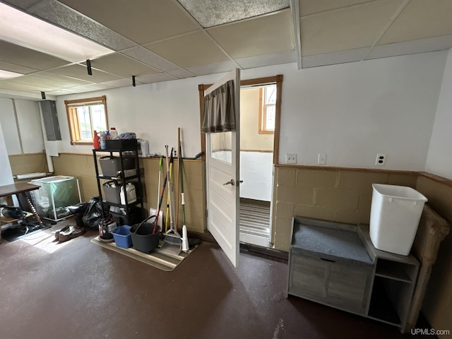 below grade area with a paneled ceiling, electric panel, and concrete block wall
