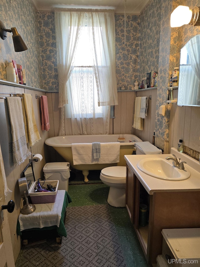 full bathroom featuring a freestanding bath, wainscoting, vanity, toilet, and wallpapered walls
