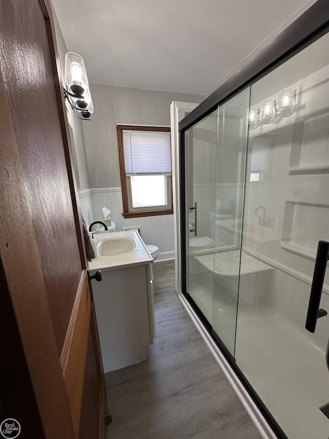 bathroom with vanity, wood finished floors, toilet, a wainscoted wall, and a shower stall