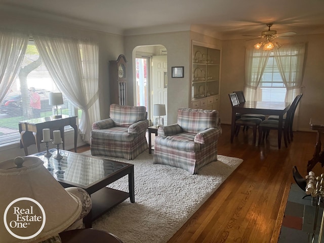 living area with arched walkways, a ceiling fan, and wood finished floors