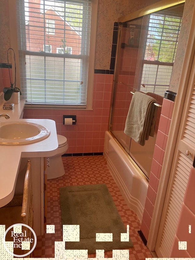 full bath featuring toilet, tile walls, a wainscoted wall, tile patterned floors, and a sink