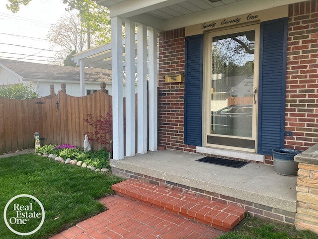 property entrance with fence, a porch, and brick siding