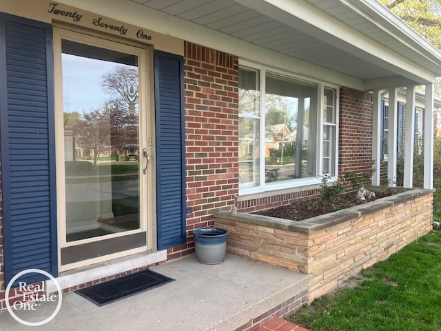 doorway to property with brick siding, visible vents, and covered porch