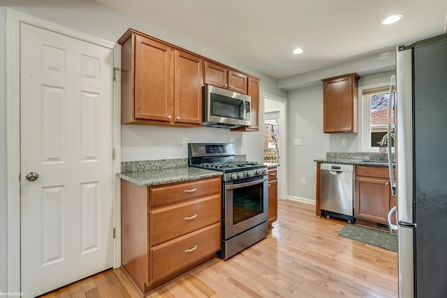 kitchen with brown cabinetry, light stone countertops, recessed lighting, light wood finished floors, and stainless steel appliances