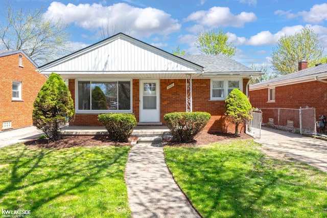 bungalow-style home with a porch, fence, a front yard, and brick siding