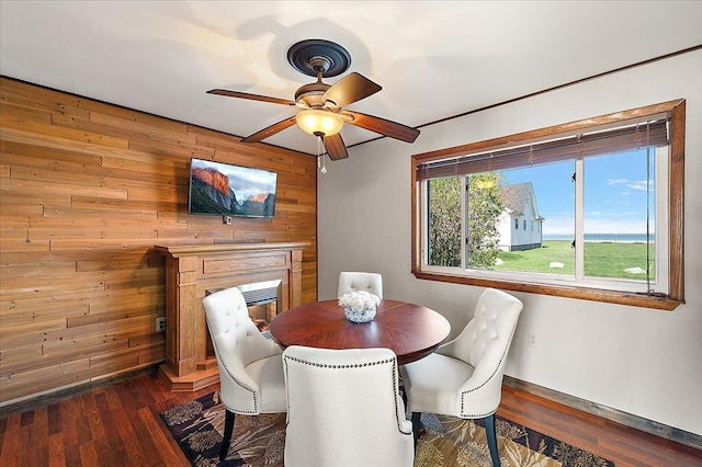dining area featuring dark wood finished floors, baseboards, ceiling fan, and wood walls
