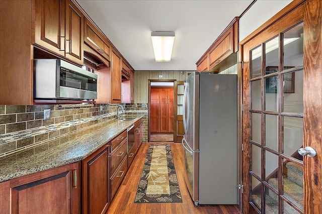 kitchen featuring appliances with stainless steel finishes, a sink, dark stone countertops, decorative backsplash, and dark wood-style floors