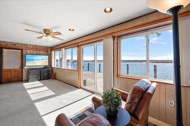 carpeted living room featuring plenty of natural light, wood walls, a ceiling fan, and visible vents