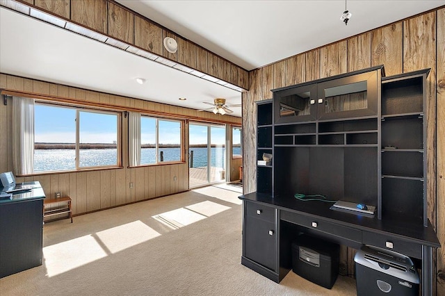 unfurnished office featuring carpet floors, a water view, a ceiling fan, and wood walls