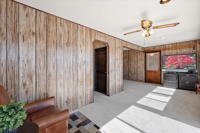 carpeted living room with ceiling fan and wood walls
