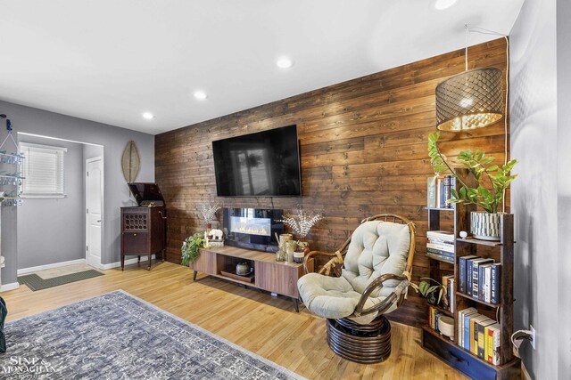 living area with wood finished floors, baseboards, wooden walls, an accent wall, and recessed lighting