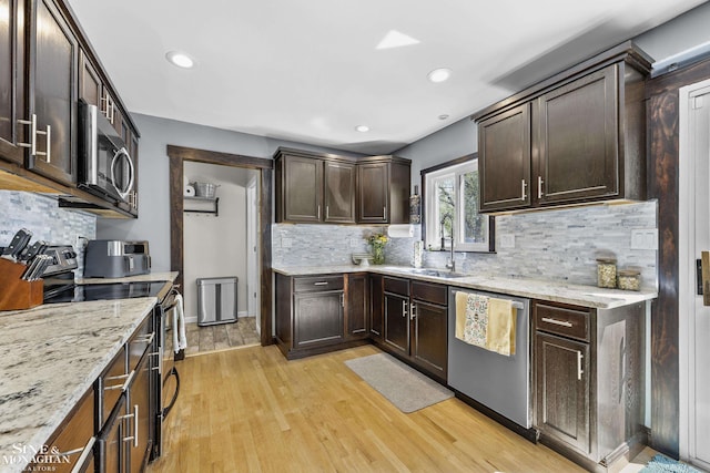 kitchen with dark brown cabinetry, appliances with stainless steel finishes, a sink, light wood-style floors, and backsplash