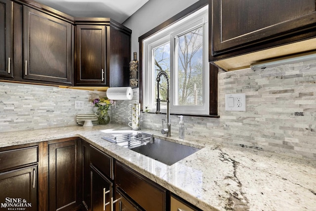 kitchen featuring backsplash, dark brown cabinets, light stone counters, and a sink