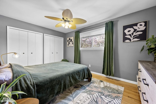 bedroom featuring two closets, a ceiling fan, baseboards, and light wood-style flooring