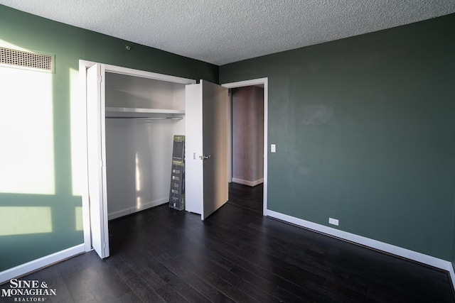 unfurnished bedroom with a textured ceiling, visible vents, baseboards, a closet, and dark wood-style floors