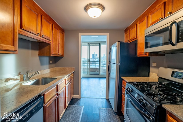 kitchen featuring baseboards, dark wood-type flooring, brown cabinets, a sink, and appliances with stainless steel finishes