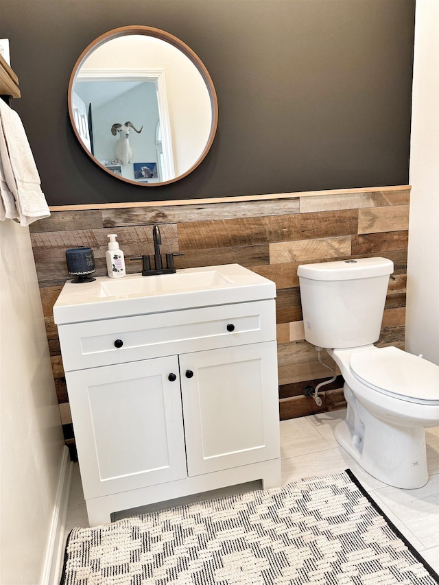 half bathroom featuring vanity, tile walls, wainscoting, and toilet