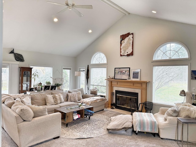 living room with beam ceiling, high vaulted ceiling, a ceiling fan, a fireplace with flush hearth, and a healthy amount of sunlight