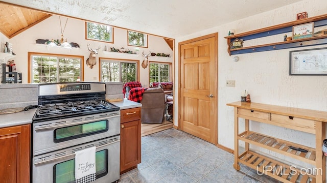 kitchen featuring brown cabinetry, open shelves, light countertops, range with two ovens, and vaulted ceiling