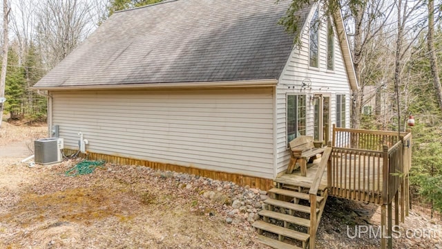 view of property exterior featuring cooling unit, a wooden deck, a shingled roof, and stairs