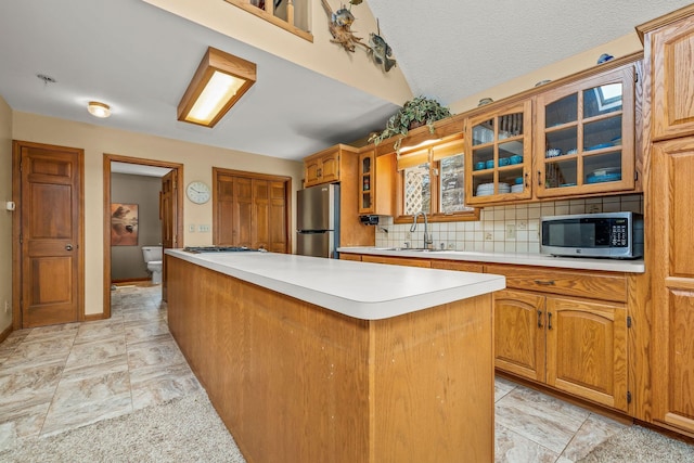 kitchen featuring glass insert cabinets, a center island, light countertops, a sink, and appliances with stainless steel finishes