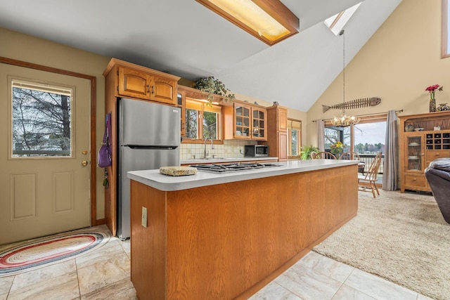kitchen with an inviting chandelier, glass insert cabinets, high vaulted ceiling, light countertops, and appliances with stainless steel finishes