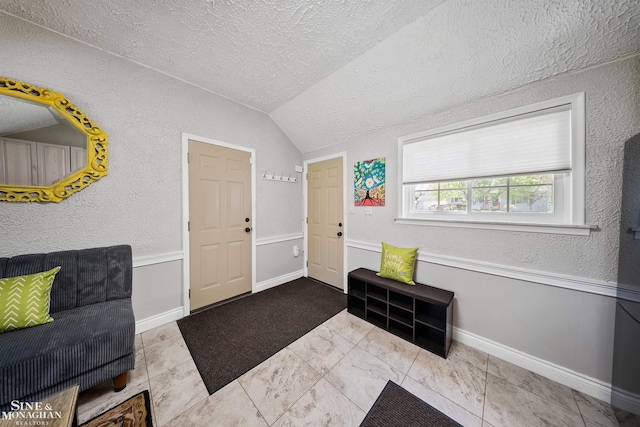foyer with baseboards, a textured ceiling, a textured wall, and vaulted ceiling