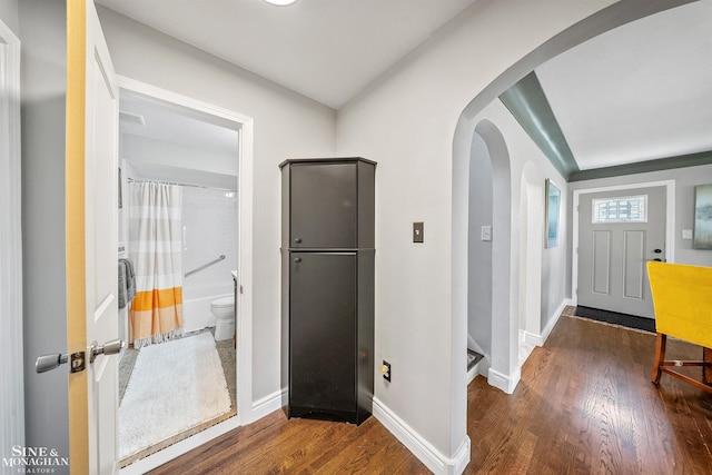 corridor featuring baseboards, arched walkways, and wood finished floors