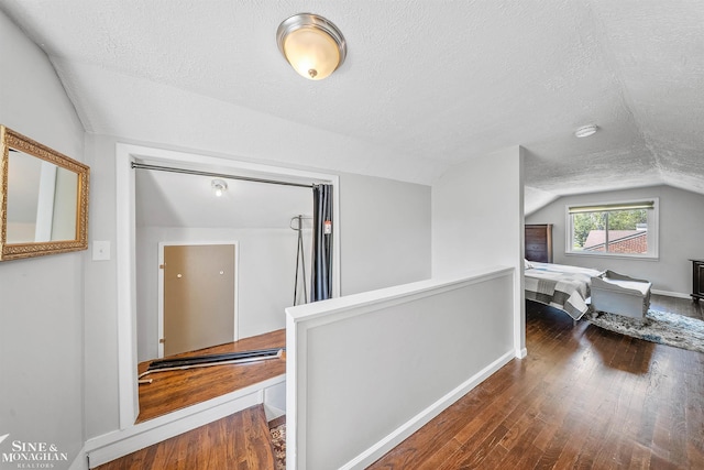 hallway featuring baseboards, a textured ceiling, lofted ceiling, and hardwood / wood-style flooring