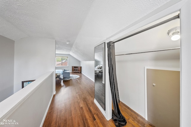 hallway featuring a textured ceiling, an upstairs landing, wood finished floors, and lofted ceiling
