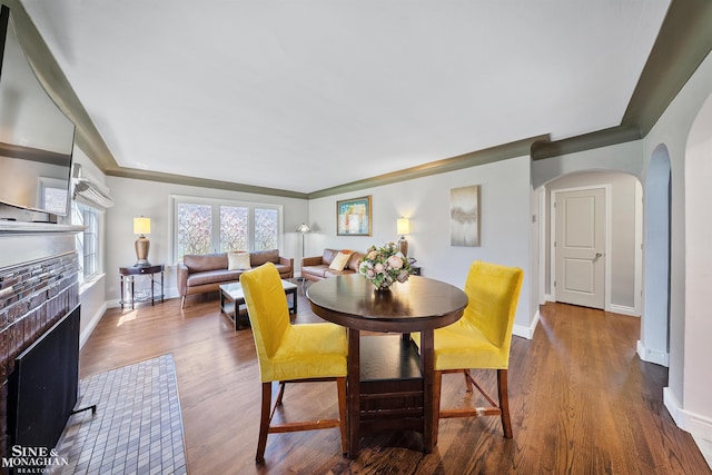 dining space featuring arched walkways, baseboards, a fireplace, and wood finished floors