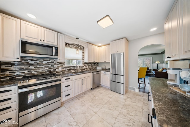 kitchen featuring visible vents, a sink, arched walkways, appliances with stainless steel finishes, and backsplash