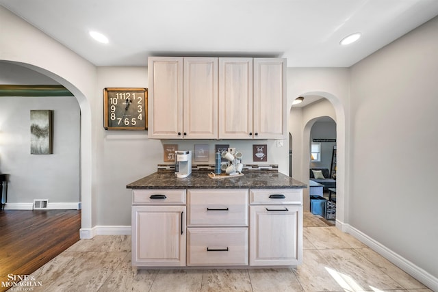 kitchen with visible vents, arched walkways, dark stone countertops, and baseboards
