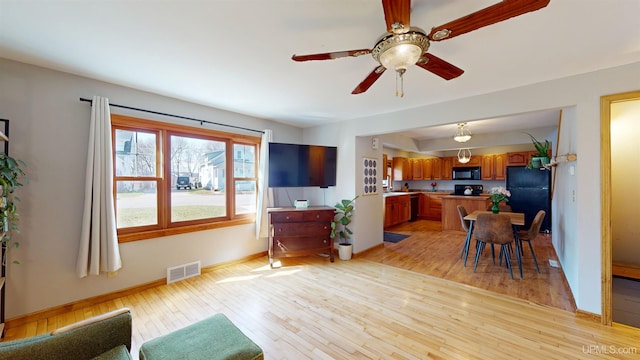 living area featuring visible vents, light wood-style floors, ceiling fan, and baseboards