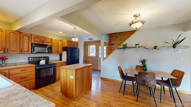 kitchen with a center island, light countertops, light wood-type flooring, black appliances, and decorative light fixtures