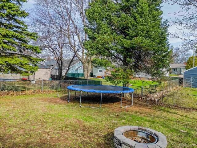 view of yard featuring fence, a trampoline, and an outdoor fire pit