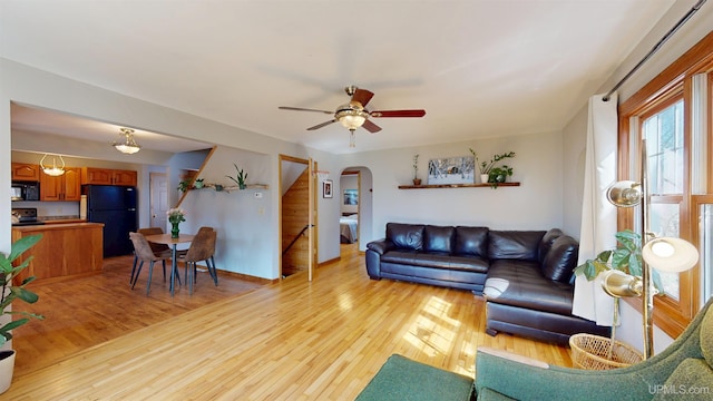 living area with arched walkways, light wood finished floors, and ceiling fan