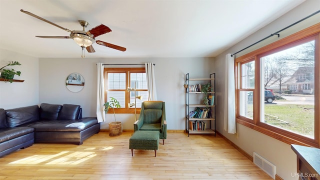 living room featuring light wood-style floors, baseboards, ceiling fan, and visible vents