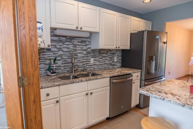 kitchen with white cabinetry, light stone counters, a sink, appliances with stainless steel finishes, and backsplash
