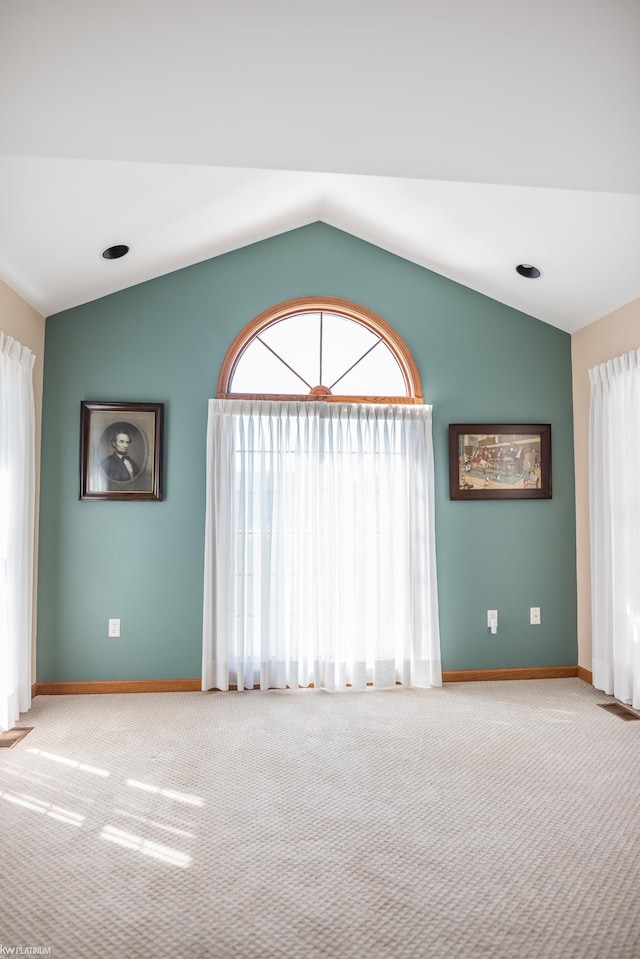 spare room featuring carpet floors, baseboards, lofted ceiling, and visible vents