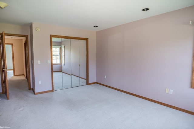 unfurnished bedroom featuring baseboards, a closet, and light carpet