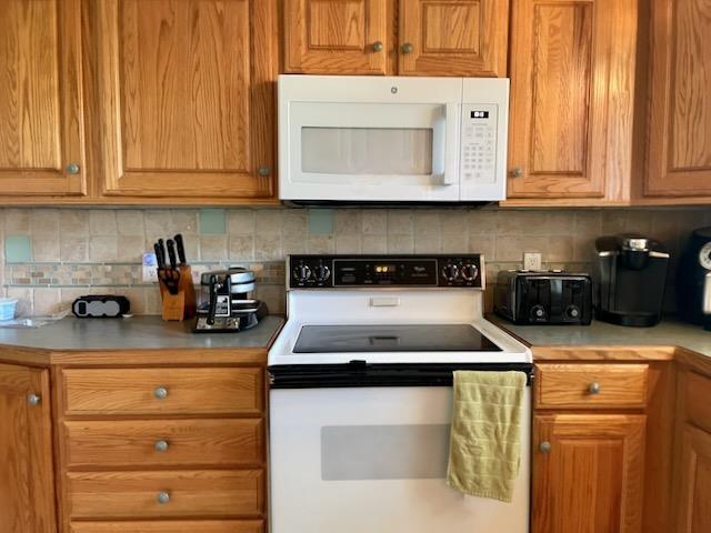 kitchen featuring backsplash, brown cabinets, light countertops, a toaster, and white appliances