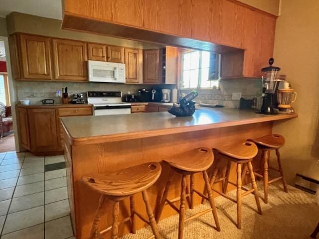 kitchen with a peninsula, decorative backsplash, brown cabinetry, and white appliances