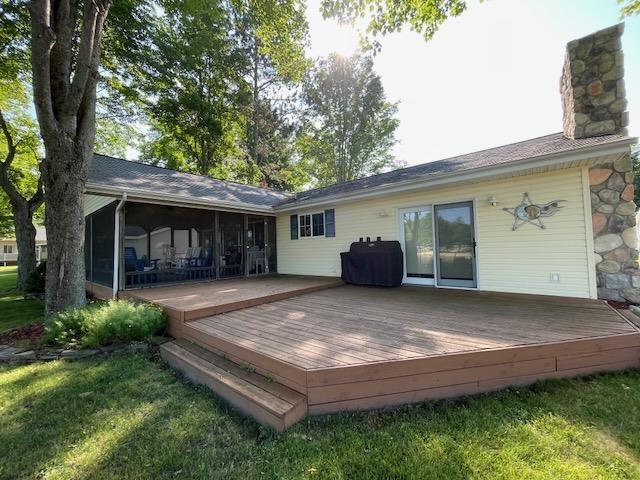 rear view of house featuring a sunroom, a wooden deck, a yard, and a chimney