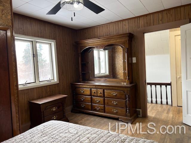 bedroom with a ceiling fan, wood walls, and wood finished floors