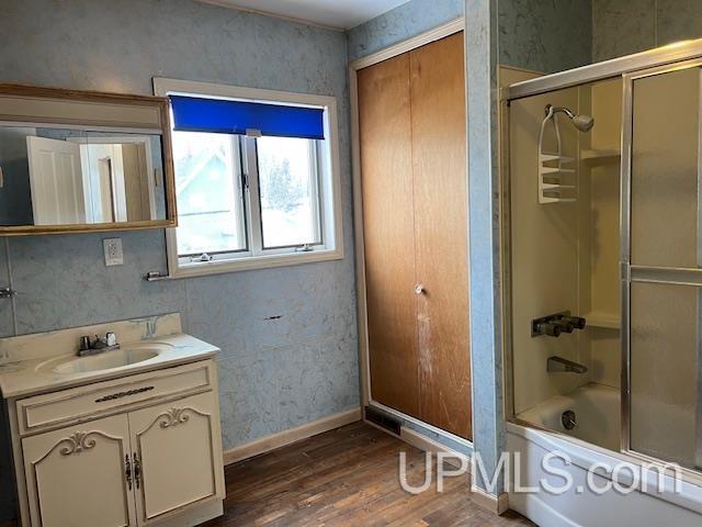 bathroom featuring vanity, baseboards, wood finished floors, and shower / bath combination with glass door