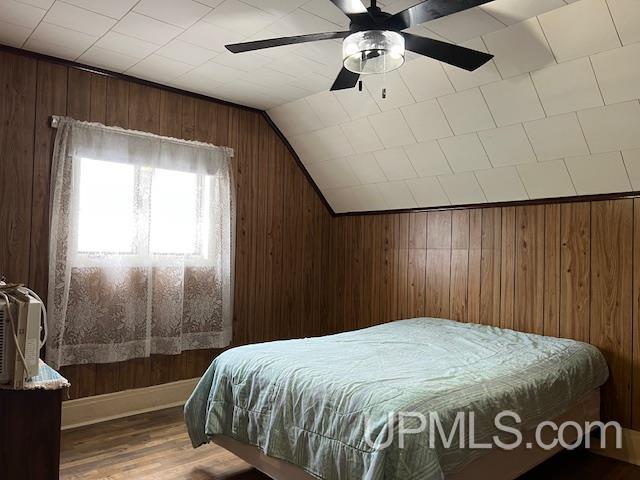 bedroom featuring a ceiling fan, vaulted ceiling, wood walls, and wood finished floors
