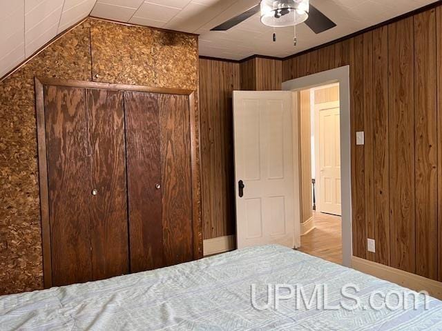 bedroom with vaulted ceiling, a ceiling fan, a closet, and wood walls