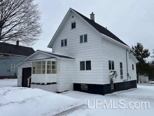 snow covered property featuring a sunroom and a chimney