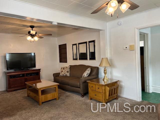 carpeted living area featuring baseboards, ornamental molding, and ceiling fan